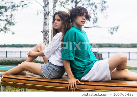 two young people, a guy and a girl, are sitting on a bench in a coastal park 105765482