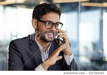 Young successful arab businessman boss talking on phone close up, man smiling contentedly inside office at workplace in business suit. Young successful arab businessman boss talking on phone close up, man smiling contentedly inside office at workplace in business suit. 105766261