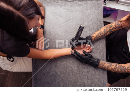 Professional tattoo artist creating airplane design on wrist of woman Professional tattoo artist creating airplane design on wrist of woman 105767339