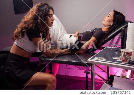 Female tattoo artist making colorful tattoo for girl in salon Female tattoo artist making colorful tattoo for girl in salon 105767341