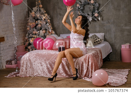 Cute woman in sexy lingerie is having fun during hen-party, sitting on bed, playing with balloon. Studio with New year tree, decorations. Close-up. Cute woman in sexy lingerie is having fun during hen-party, sitting on bed, playing with balloon. Studio with New year tree, decorations. Close-up. 105767374