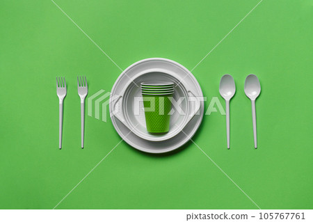 Colorful plastic disposable tableware on green background with copy space. The concept of picnic utensil. Top view. Selective focus. Close-up. 105767761