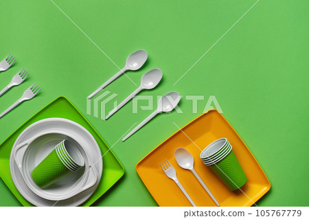 Colorful plastic disposable tableware on green background with copy space. The concept of picnic utensil. Top view. Selective focus. Close-up. Colorful plastic disposable tableware on green background with copy space. The concept of picnic utensil. Top view. Selective focus. Close-up. 105767779