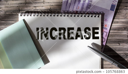 Text on a white sheet. Increase Income. On a wooden table is the euro. Currency, stickers and pen. Text on a white sheet. Increase Income. On a wooden table is the euro. Currency, stickers and pen. 105768863