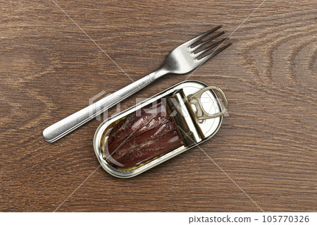 Opened tin can of anchovy fillet in oil and silver fork on a wooden background 105770326