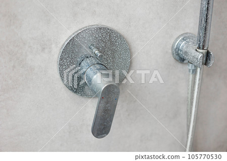 Dirty calcified shower mixer tap, faucet with limescale on it, plaque from hard water, Chrome plated shower, close up photo. Bathroom with grey tiles interior. 105770530