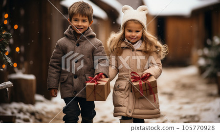 Cute Couple of Children Dressed Warmly Holding a Wrapped Christmas Gift Outdoors. 105770928