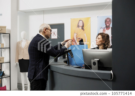 Senior customer taking shopping bag from boutique worker, after buying fashionable clothes in shopping centre. Elderly shopper paying for stylish merchandise during commercial activity 105771414