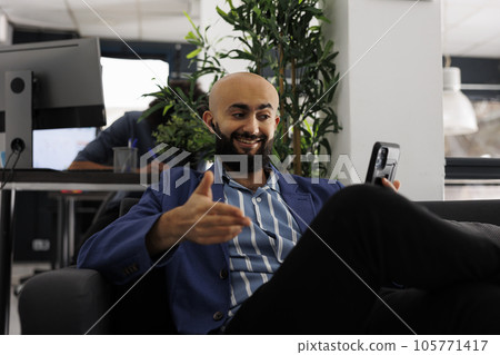 Arab smiling businessperson using smartphone videocall app to manage company sales and marketing strategy with coworkers. Executive discussing project during an online meeting Arab smiling businessperson using smartphone videocall app to manage company sales and marketing strategy with coworkers. Executive discussing project during an online meeting 105771417