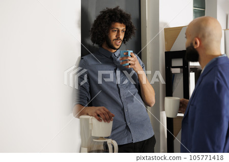 Arab coworkers having conversation while drinking coffee and standing in business office. Two colleagues discussing company start up project during work break in coworking space Arab coworkers having conversation while drinking coffee and standing in business office. Two colleagues discussing company start up project during work break in coworking space 105771418