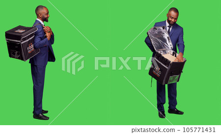 Male takeout employee in suit having meal order, carrying thermal bag with fast food. Deliveryman being stylish and confident delivering takeaway food, full body greenscreen backdrop. Male takeout employee in suit having meal order, carrying thermal bag with fast food. Deliveryman being stylish and confident delivering takeaway food, full body greenscreen backdrop. 105771431