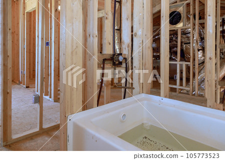 Under construction house featuring new acrylic bathtub between beams frame in a bathroom Under construction house featuring new acrylic bathtub between beams frame in a bathroom 105773523