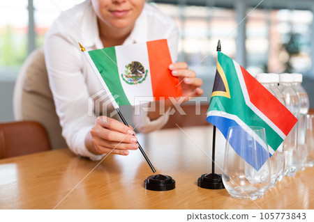 Woman secretary prepares an office for negotiations - she places flags of South Africa and Mexico table Woman secretary prepares an office for negotiations - she places flags of South Africa and Mexico table 105773843