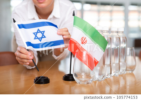 Woman secretary prepares an office for negotiations - she places flags of Iran and Israel table 105774153