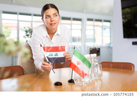 Woman secretary prepares an office for negotiations - she places flags of Iraq and Iran table Woman secretary prepares an office for negotiations - she places flags of Iraq and Iran table 105774185