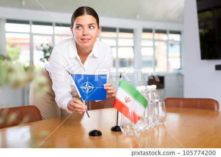 Woman secretary prepares an office for negotiations - she places flags of NATO (OTAN) and Iran table Woman secretary prepares an office for negotiations - she places flags of NATO (OTAN) and Iran table 105774200