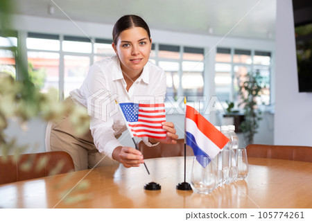 Young woman puts USA and Netherlands flags on table in office Young woman puts USA and Netherlands flags on table in office 105774261