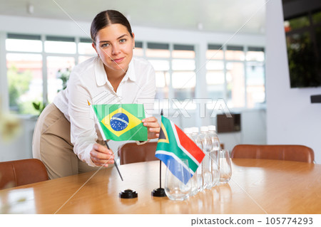 Young lady sets miniatures flags of South Africa and Brazil for international negotiations 105774293