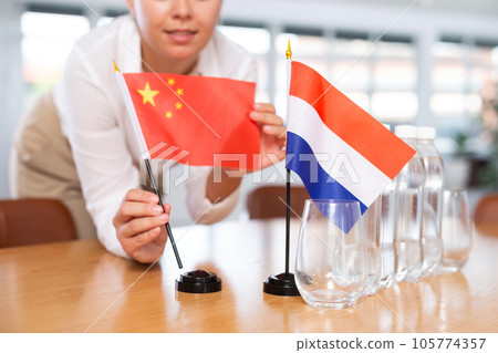Young woman putting flags of China and Netherlands on table in office 105774357
