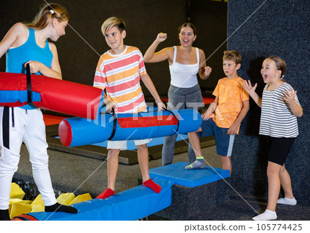 Happy child school boy and teenage girl friends fighting by inflatable logs while spending weekend together in entertainment center 105774425