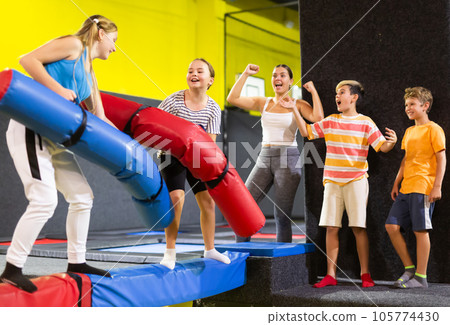Active excited child school girls having fun and fighting with inflatable logs in amusement center 105774430