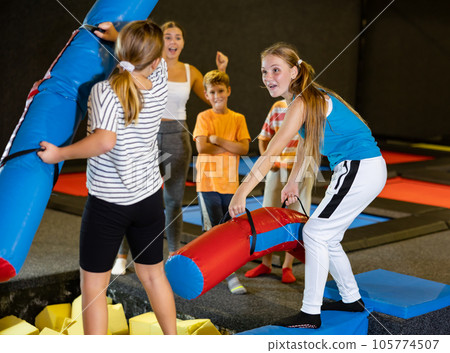 Teenage girl fighting by pugil sticks with little sister on inflatable beam Teenage girl fighting by pugil sticks with little sister on inflatable beam 105774507