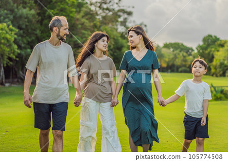 A loving family enjoying a leisurely walk in the park - a radiant pregnant woman after 40, embraced by her husband, and accompanied by their adult teenage children, savoring precious moments together A loving family enjoying a leisurely walk in the park - a radiant pregnant woman after 40, embraced by her husband, and accompanied by their adult teenage children, savoring precious moments together 105774508