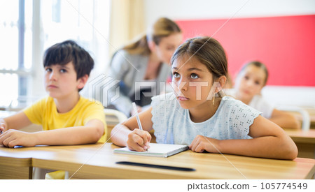 Concentrated tween girl listening to schoolteacher and writing in notebook 105774549