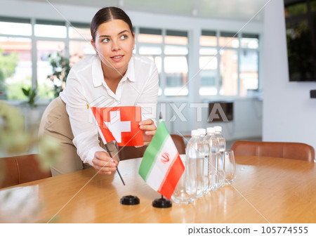 Positive young woman putting little flag of Switzerland on table next to the flag of Iran Positive young woman putting little flag of Switzerland on table next to the flag of Iran 105774555