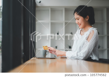 Young woman holding credit card and using laptop computer. Businesswoman working at home. Online shopping, e-commerce, internet banking, spending money. 105774562