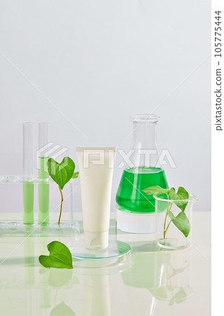 Unbranded tube placed on a podium decorated with a conical flask, test tubes and a beaker of fish mint leaves. Fish mint (Houttuynia cordata) contains antibacterial ingredients 105775444