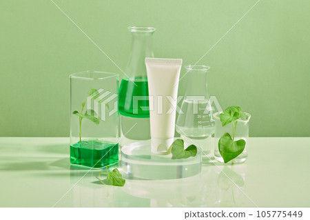 White tube without label standing on the podium with glassware of liquid surrounded. Fish mint (Houttuynia cordata) mask is used by many women to treat hidden acne 105775449