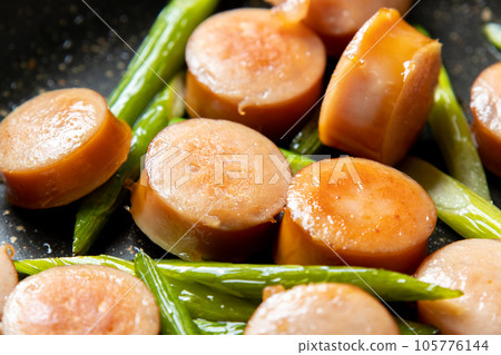 A cooking scene where frankfurter sausage and garlic sprouts are fried. 105776144