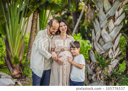 A loving family enjoying a leisurely walk in the park - a radiant pregnant woman after 40, embraced by her husband, and accompanied by their adult teenage son, savoring precious moments together 105776537