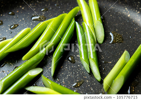 A cooking scene where garlic sprouts (diagonally cut) are fried in a frying pan. 105776715