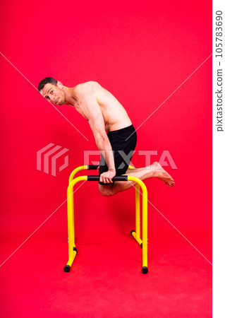 Young muscular man doing parallel bar exercises in dark white red studio with copy space 105783690