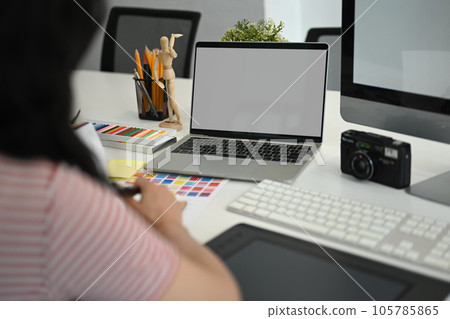 View over shoulder of female freelancer sitting at modern workplace and working with color swatch sample 105785865