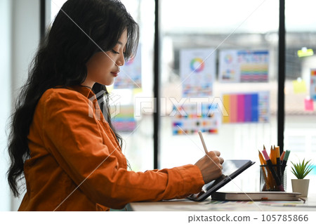 Side view of concentrated young creative woman working on project, using digital tablet at office 105785866