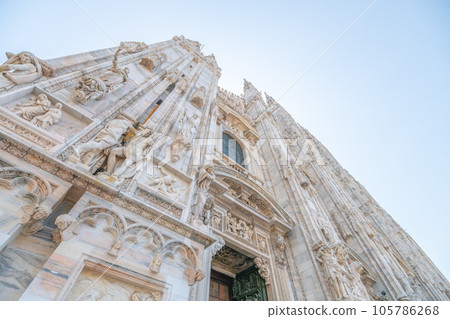 Milan Cathedral, Italian: Duomo di Milano, or Metropolitan Cathedral-Basilica of the Nativity of Saint Mary. View of main door and white marble facade on sunny summer day. Milan, Lombardy, Italy 105786268