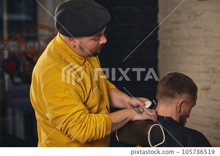 Barber making haircut of attractive bearded man in barbershop 105786519