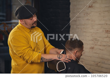 Barber making haircut of attractive bearded man in barbershop Barber making haircut of attractive bearded man in barbershop 105786520