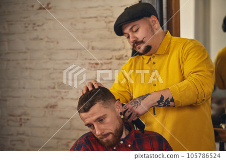 Barber making haircut of attractive bearded man in barbershop Barber making haircut of attractive bearded man in barbershop 105786524