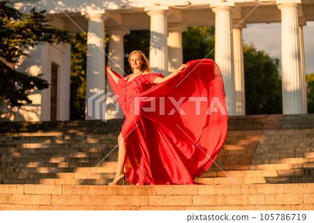 A woman in a long red dress against the backdrop of sunrise, bright golden light of the sun's rays. The concept of femininity, harmony. 105786719