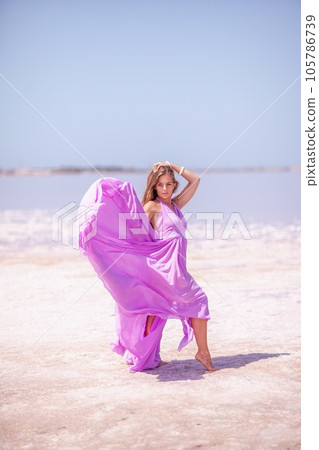 Woman pink salt lake. Against the backdrop of a pink salt lake, a woman in a long pink dress takes a leisurely stroll along the white, salty shore, capturing a wanderlust moment. 105786739