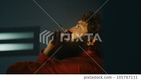 Pensive male prisoner smokes cigarette in prison cell Pensive male prisoner smokes cigarette in prison cell 105787131