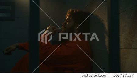Depressed male prisoner sits on the bed, smokes cigarette in prison cell Depressed male prisoner sits on the bed, smokes cigarette in prison cell 105787137