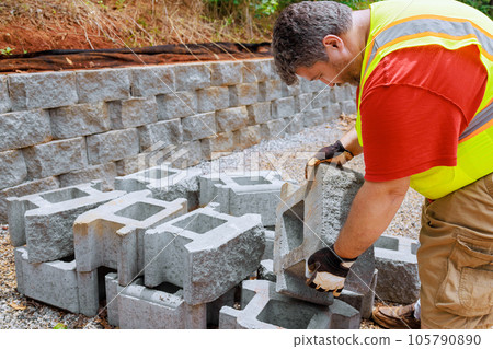 Construction worker lifts concrete block and places it on retaining wall 105790890