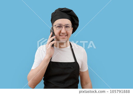 Portrait of a smiling chef with a phone in his hands looking at the camera on a blue background. Portrait of a smiling chef with a phone in his hands looking at the camera on a blue background. 105791888
