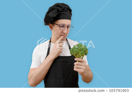 Thoughtful cook with broccoli in his hand on a blue background. Cooking and people concept 105791903