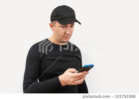 Young man in a baseball cap using a phone on a white background. 105791986